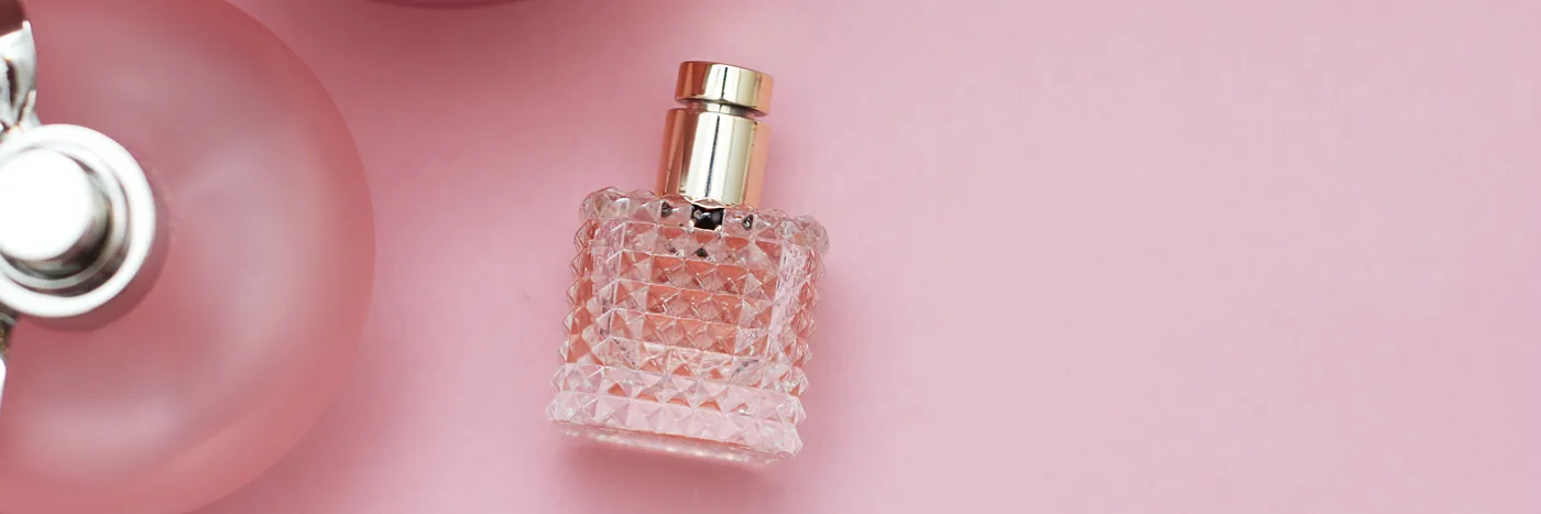 A close overhead view of several unbranded frosted and cut glass perfume bottles on a pink surface.
